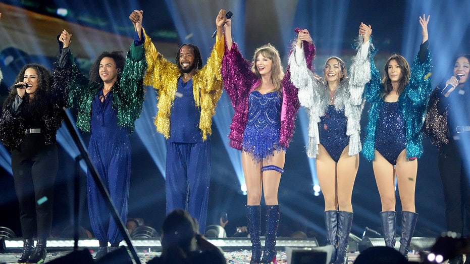 Taylor Swift holds hands in the air with her dancers as they get ready to take a bow at the end of The Eras Tour concert in Santa Clara